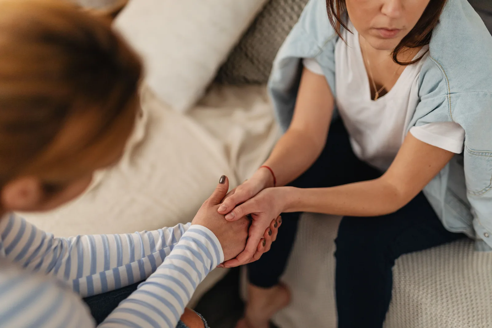 Twee vrouwen zitten tegenover elkaar op een bank en houden elkaars handen vast